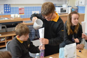 Two young people and a youth worker sit at a classroom table, building bird feeders with paper funnels and plastic water bottles.