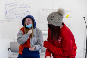 Two young people stand in front of a whiteboard, laughing.