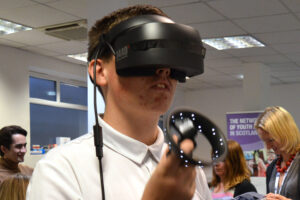 A young person wears a VR headset and attempts to drive a vehicle