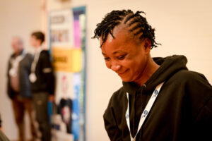 A young person in a black sweatshirt and Youth Scotland lanyard smiles in an auditorium.