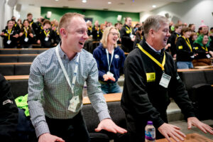 Keith Brown, Youth Scotland employees, and a large group of young people stand in an auditorium following along in an energiser.