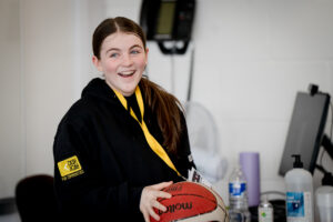 A young person wearing a black CashBack for Communities sweatshirt catches a basketball and smiles.