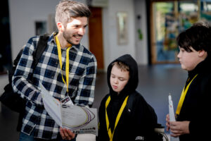 A youth worker smiles as they engage with two young people, gesturing to a page in a Hi5 Awards challenge sheet.