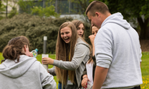 A group of young people are gathered outdoors. They are smiling as they work on a project.