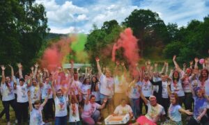 A group of young people and youth workers cheer and throw coloured dust into the air
