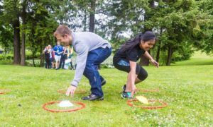 Two young people engaged in a relay reach for colourful lawn markers on a grassy field.