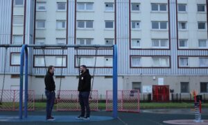 Two youth workers stand in front of a swing set in the empty playground of a block of flats.