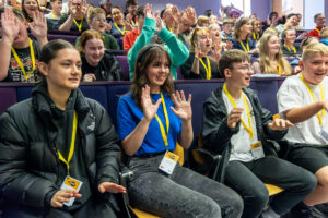 An auditorium packed with young people and youth workers enjoy an energiser activity amongst rows of seats