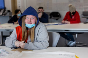 A young person sits at a classroom table writing.