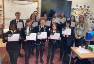 A group of young people from Alva Academy stand in a classroom holding up youth award certificates.